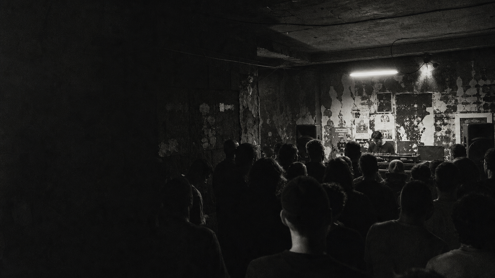 An underground music room filled with silhouettes and a performer under a fluorescent light
